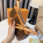 Hand holding a Louis Vuitton handbag with monogram pattern and orange accents, with brand boxes in the background.