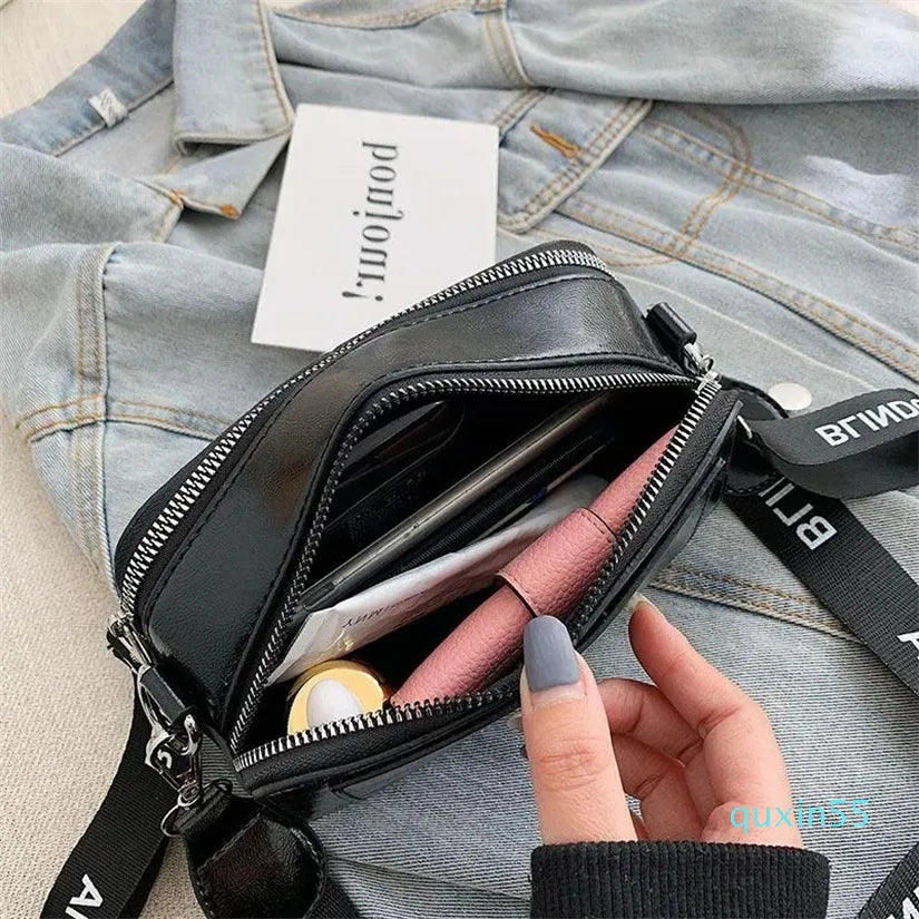 Black crossbody bag with a hand holding it open, denim jacket in the background