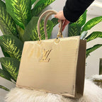Gold handbag with brand logo on a fluffy white surface with green plants in the background