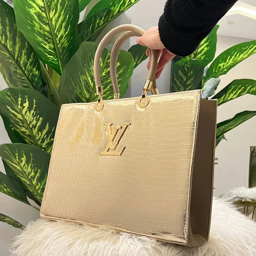 Gold handbag with brand logo on a fluffy white surface with green plants in the background