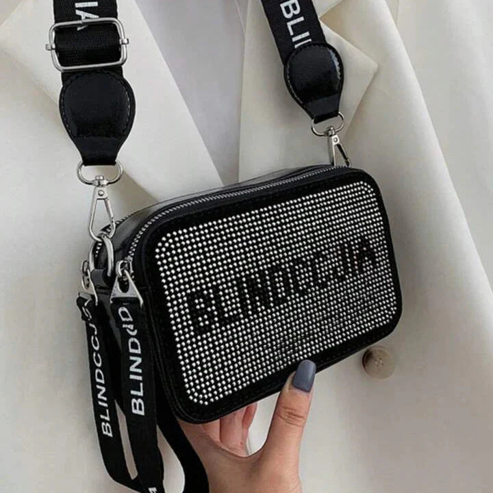 Black studded handbag with 'BLINDCIA' branding held by a hand against a white background