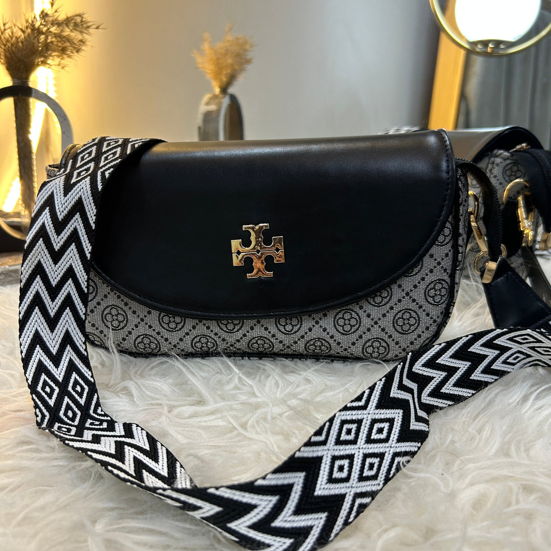 Designer handbag with a patterned strap on a reflective surface