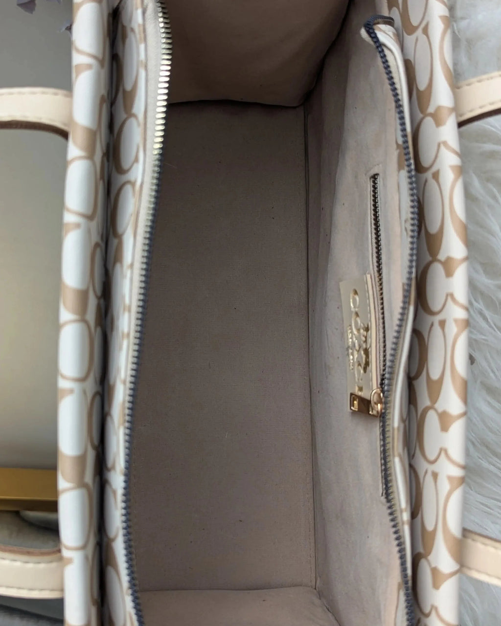 Close-up of a beige handbag with a visible brand logo on a neutral background