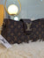 Designer handbag with monogram pattern on a fluffy surface, with a blurred indoor background.