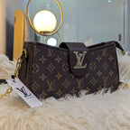 Designer handbag with monogram pattern on a fluffy surface, with a blurred indoor background.