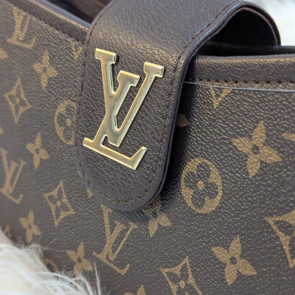 Close-up of a brown leather handbag with gold monogram pattern and logo.