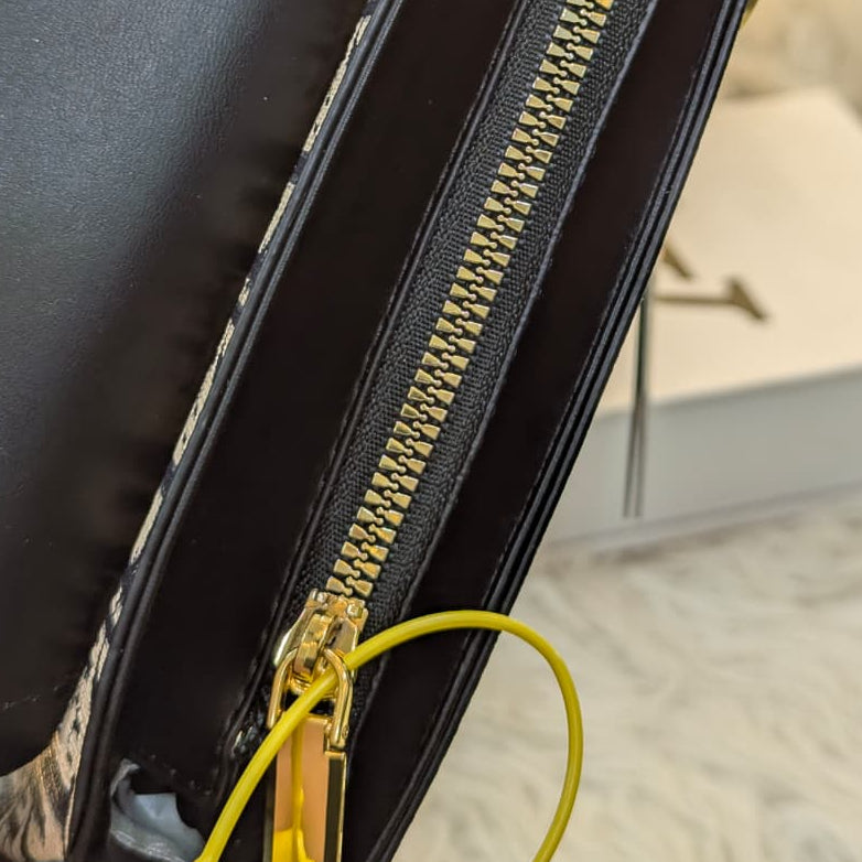 Close-up of a black handbag with a gold zipper on a blurred background