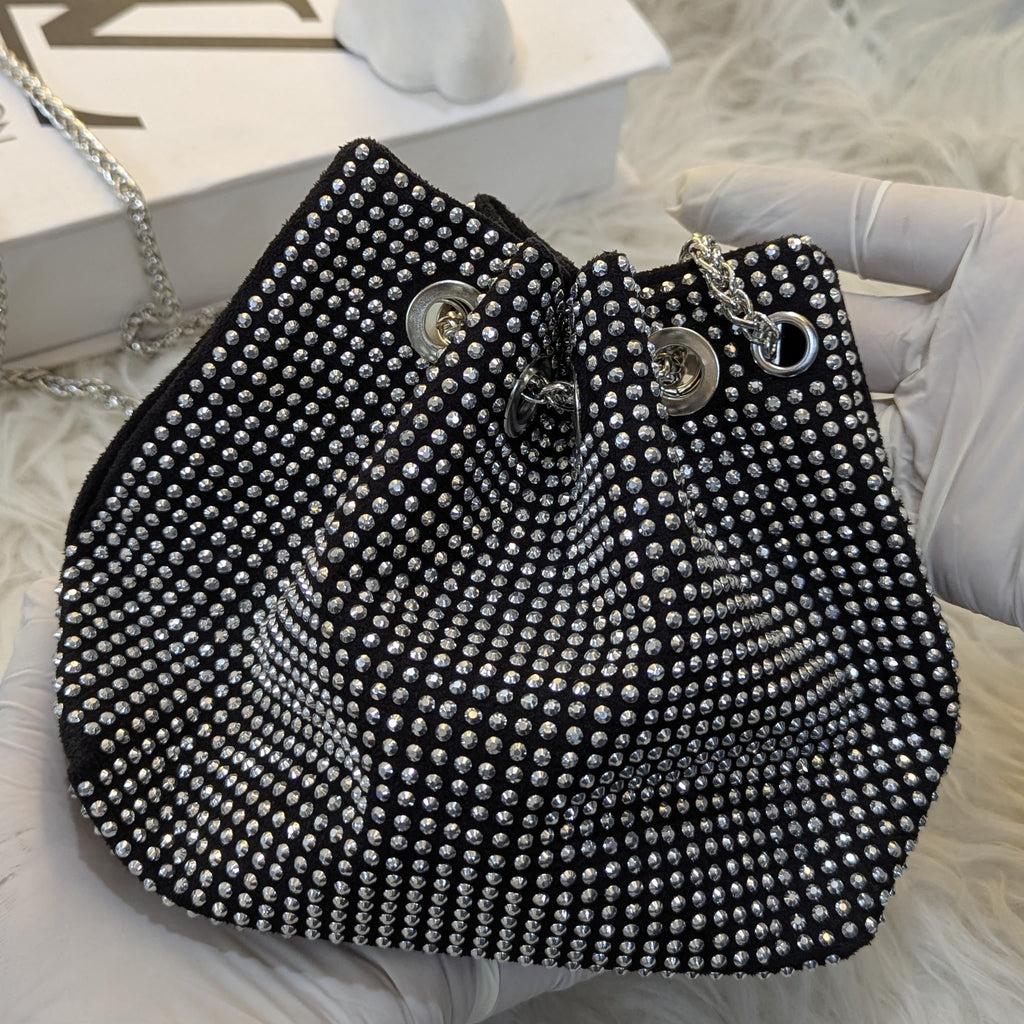 Black beaded handbag held by a gloved hand on a textured surface