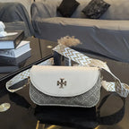 White handbag with patterned strap on a reflective surface, with books and a couch in the background.