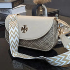 Tory Burch handbag with a patterned strap on a reflective surface