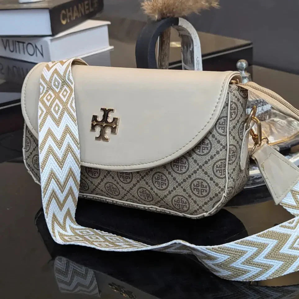 Tory Burch handbag with a patterned strap on a reflective surface