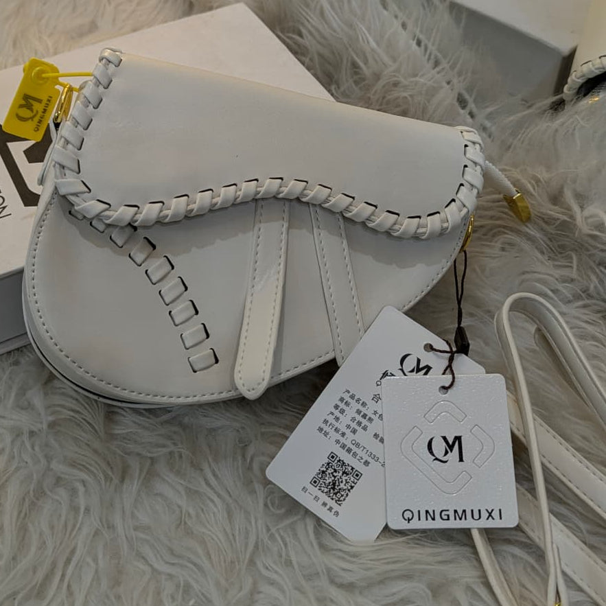 White handbag with braided handle on a fluffy white surface, featuring a QINGMUXI tag.