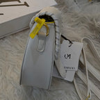 White handbag with a yellow tag on a textured surface, with a Louis Vuitton box in the background.