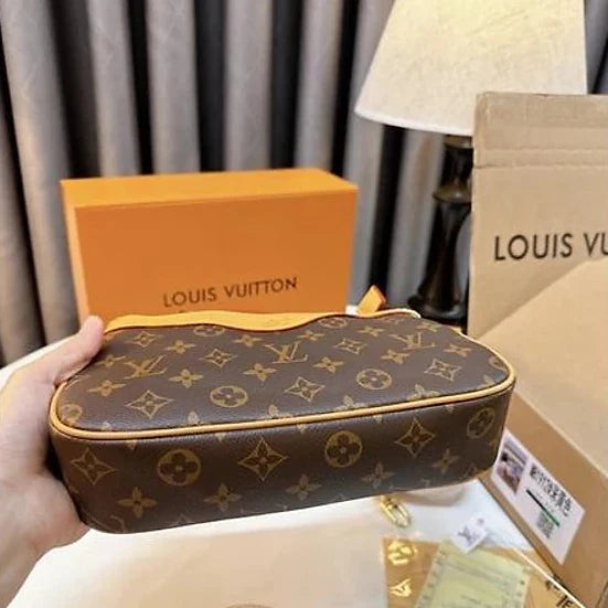 Louis Vuitton pouch held by a hand with brand packaging in the background